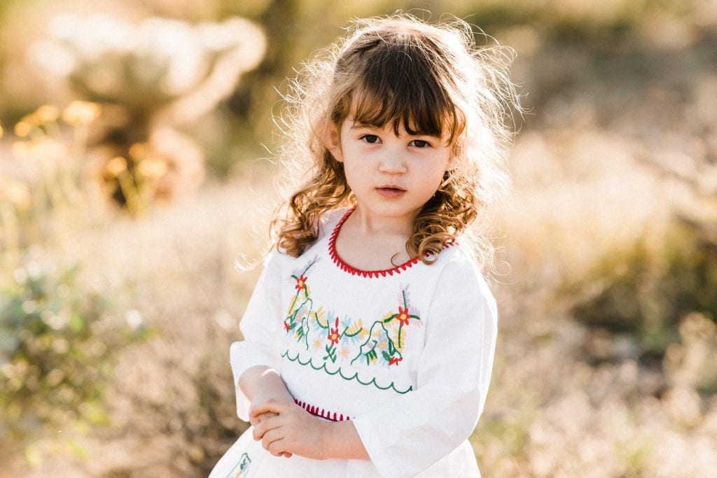 A little girl in a white dress with floral embroidery.
