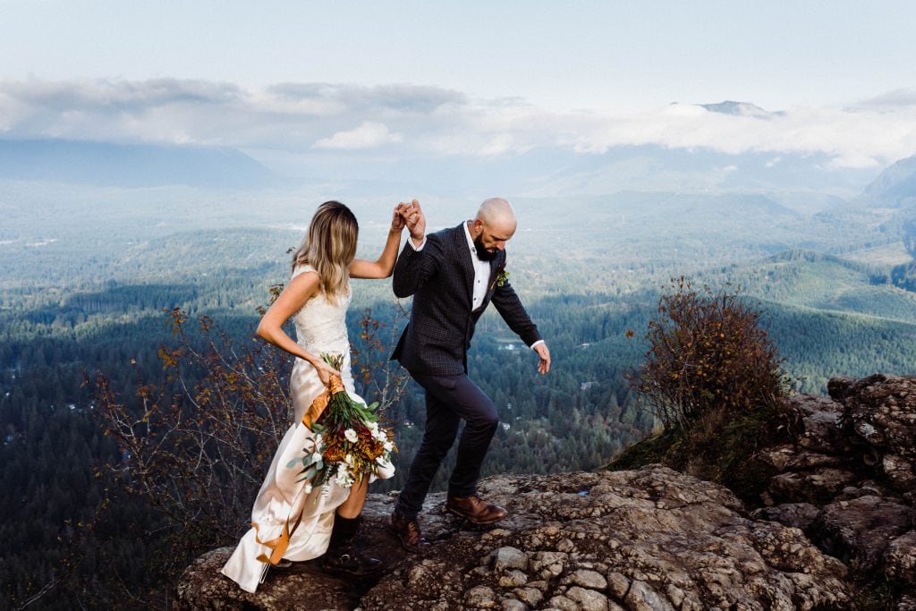 An adventurous wedding couple walking across some boulders at Rattlesnake Ledge overlook in North Bend, Washington.
