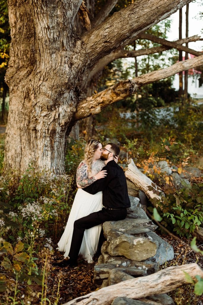 A couple kissing during their elopement under a giant tree in an old New Hampshire forest.