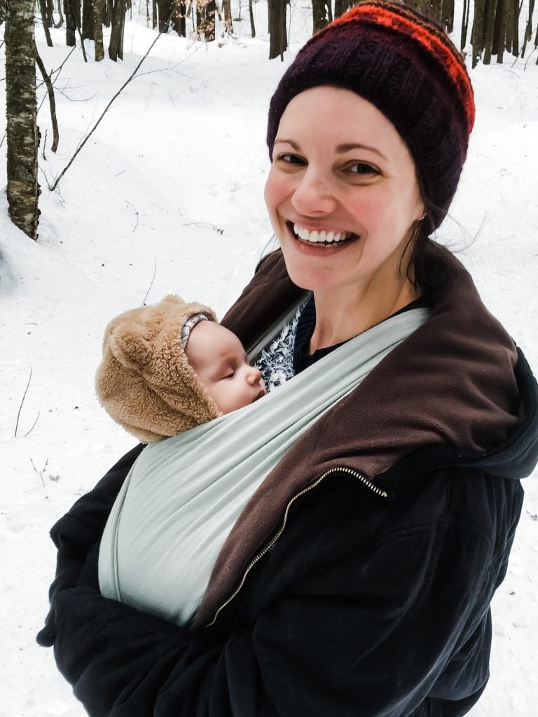 Newborn carried in a Solly baby wrap during a snowy hike