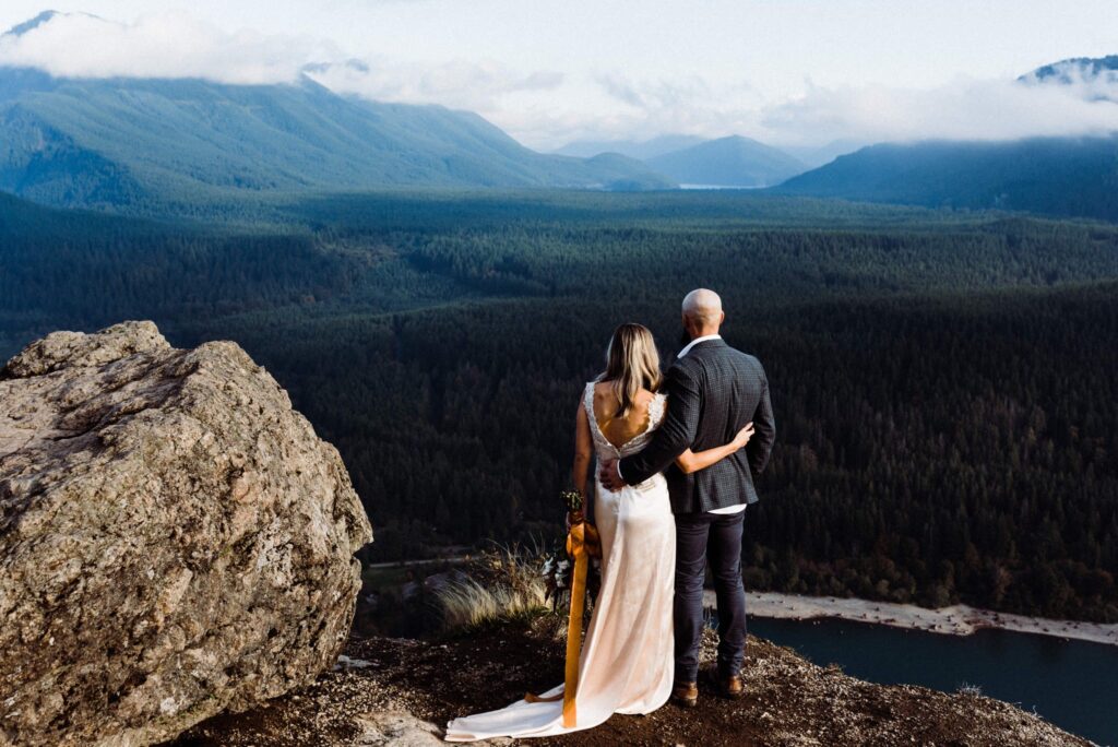 Wedding couple gazing at a mountain range during their adventurous elopement at Rattlesnake Ledge in North Bend, Washington.