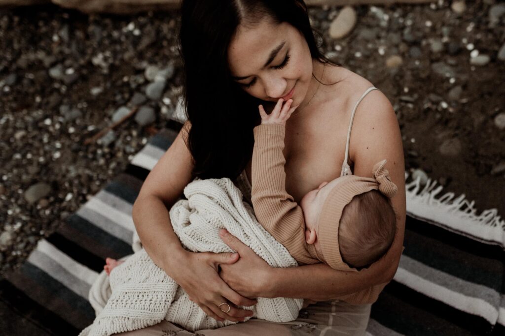 Baby touching mother's face while breastfeeding during Seattle family photography session on the beach.